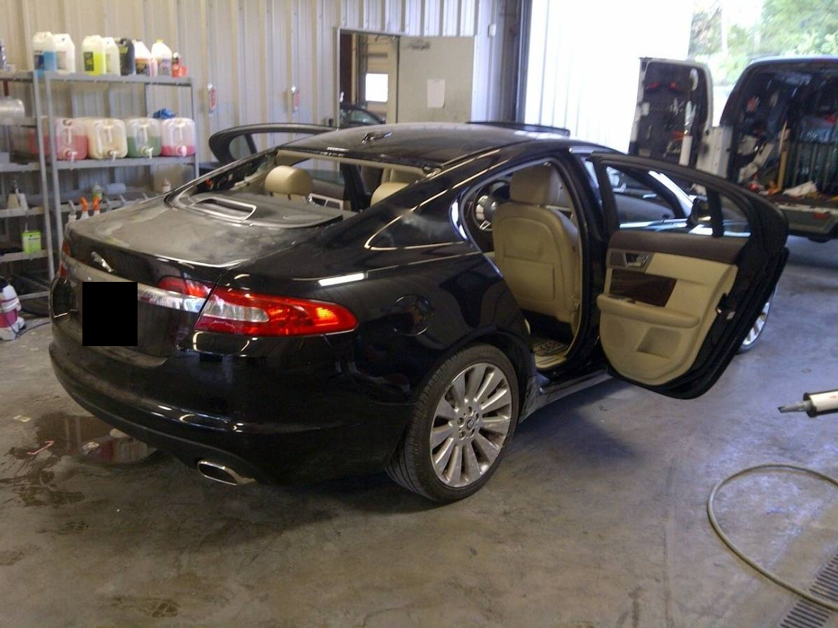 A black sedan in a workshop with its rear glass removed and rear license plate obscured.