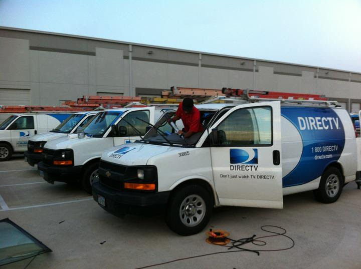 Technician working on the windshield of a DirecTV-branded van.