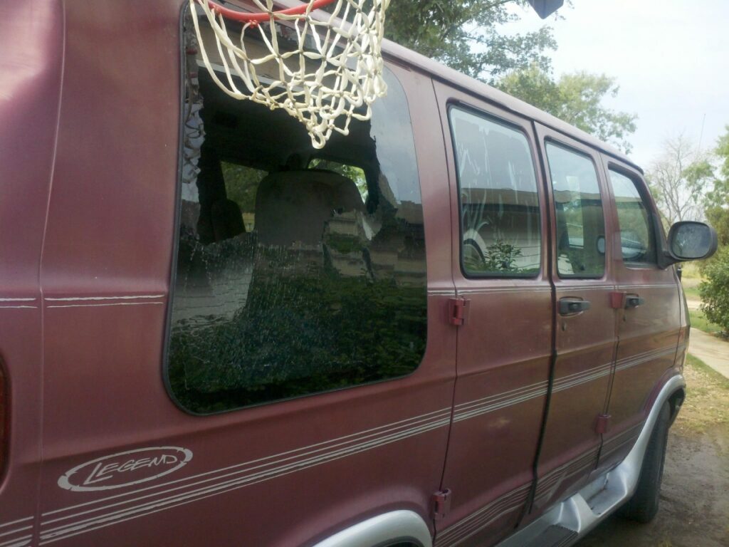 Maroon passenger van with a large hole in its shattered rear side window.