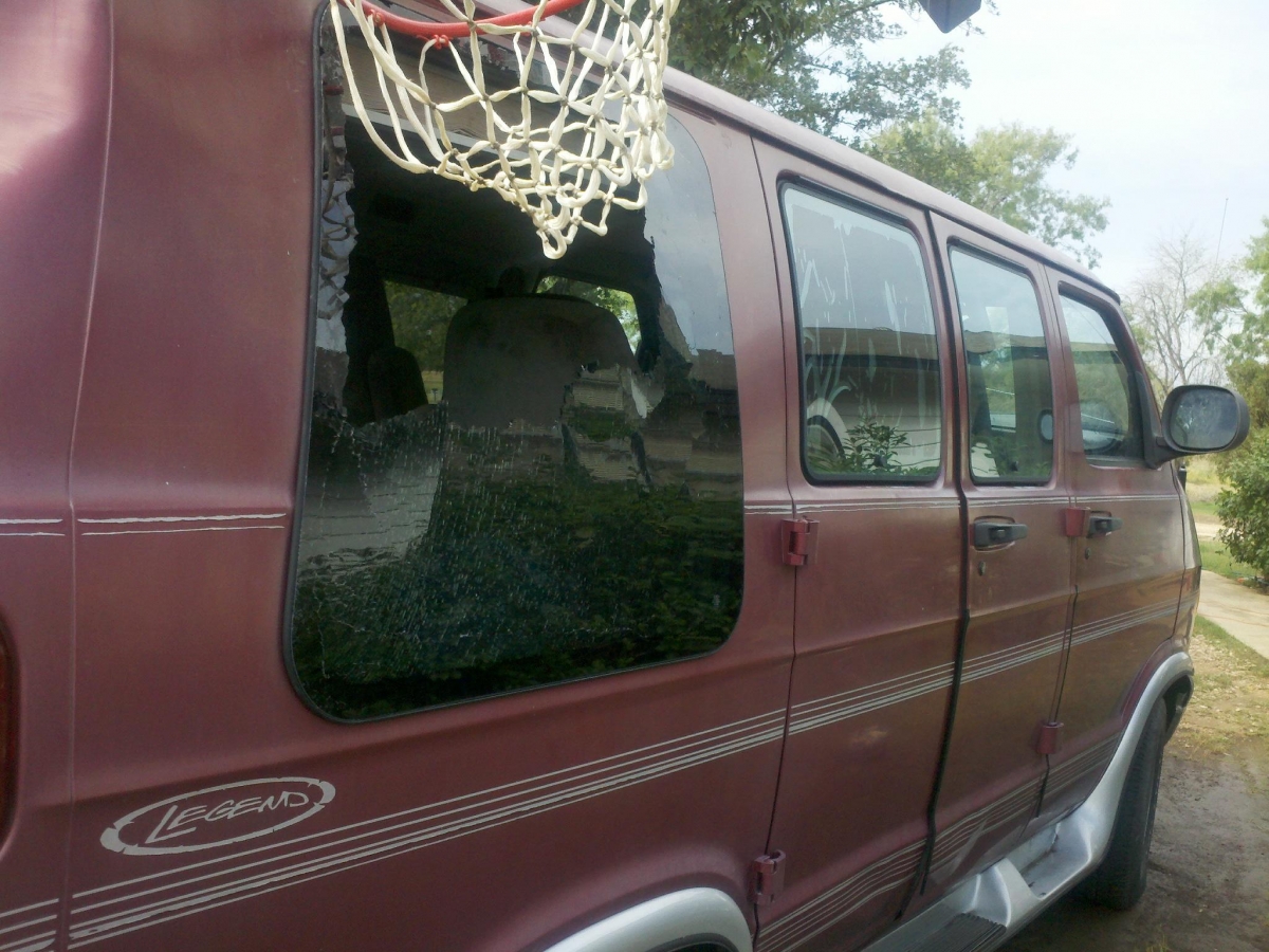 Maroon passenger van with a large hole in its shattered rear side window.