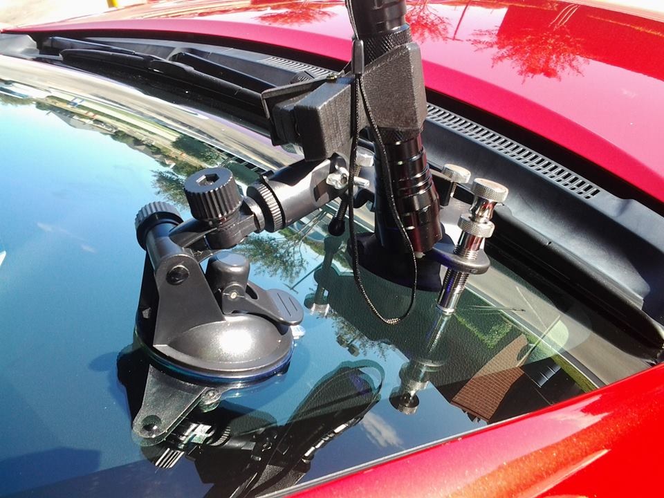 A suction-mounted windshield chip-repair injector on the glass of a red vehicle.
