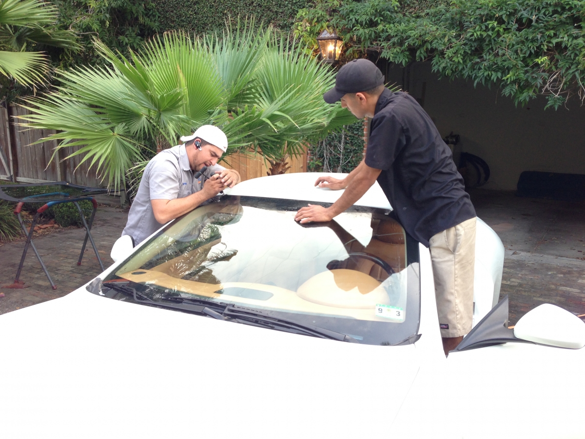 Two technicians working along the windshield edge of a white Maserati.
