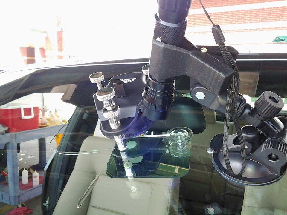 Close-up of a suction-mounted chip-repair injector with a backing mirror behind the windshield.